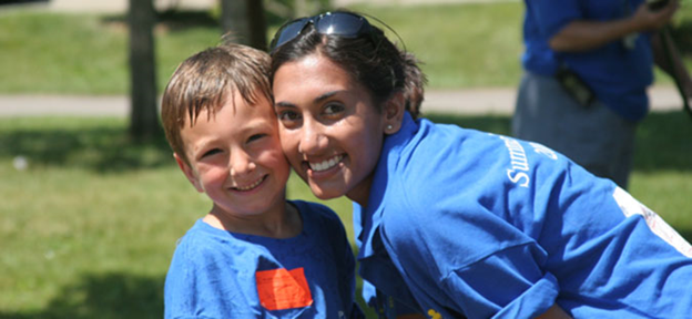 A student and child stand outside and smile at the camera