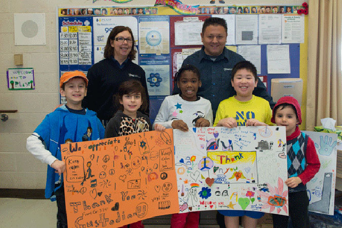 Five PLASP children present a giant thank you card to a pair of school custodians.