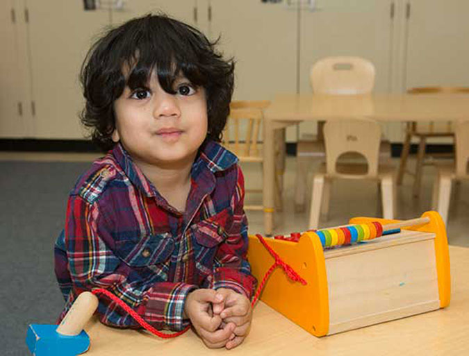 A boy poses for a photo next to a wooden toy cash register in a PLASP program 