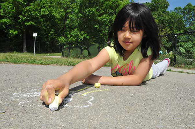 A girl draws on the asphalt with a piece of white chalk
