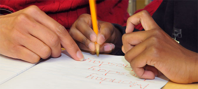 A child writing with the assistance of PLASP staff