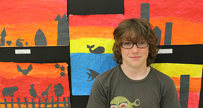 A boy poses in front of several pieces of child created artwork