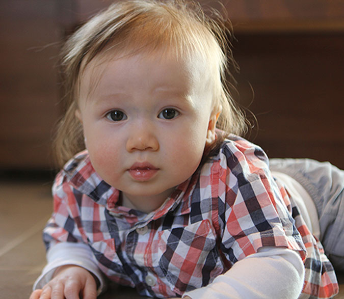 An infant wearing a plaid shirt is seen crawling