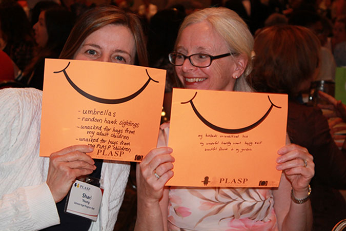 Two PLASP staff hold up orange cards with orange smiles on them