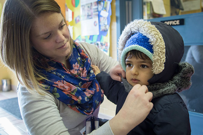 A staff members helps a child get ready for outdoor play