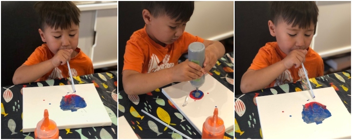 Child using a straw to blow paint on paper