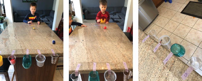 children rolling balls into cups taped to counter